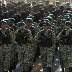 Національний прапор Ірану на фоні американських військових техніки